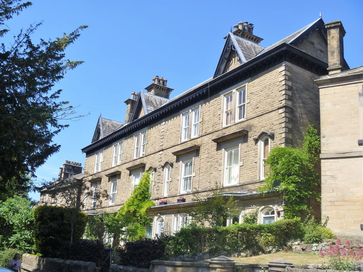A three-storey Victorian stone terrace with climbing plants on Knowleston Place in Matlock
